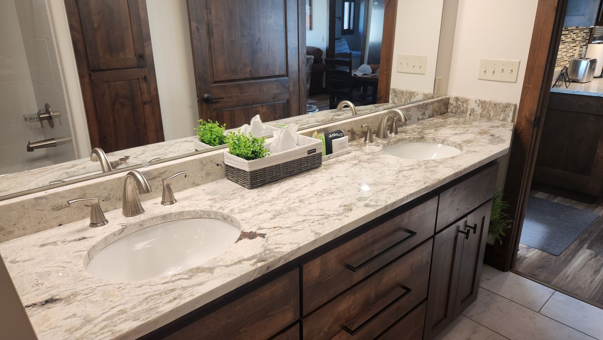 Bathroom with a double vanity, granite countertop, and wooden cabinets. Mirror reflects another room.