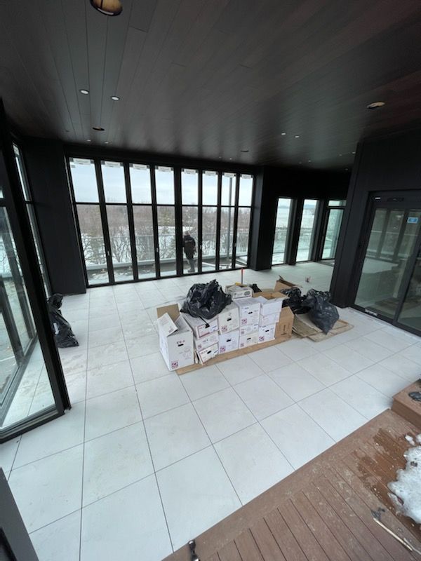 Un balcon intérieur avec un sol carrelé blanc, des baies vitrées et des cartons qui attendent d'être déballés.