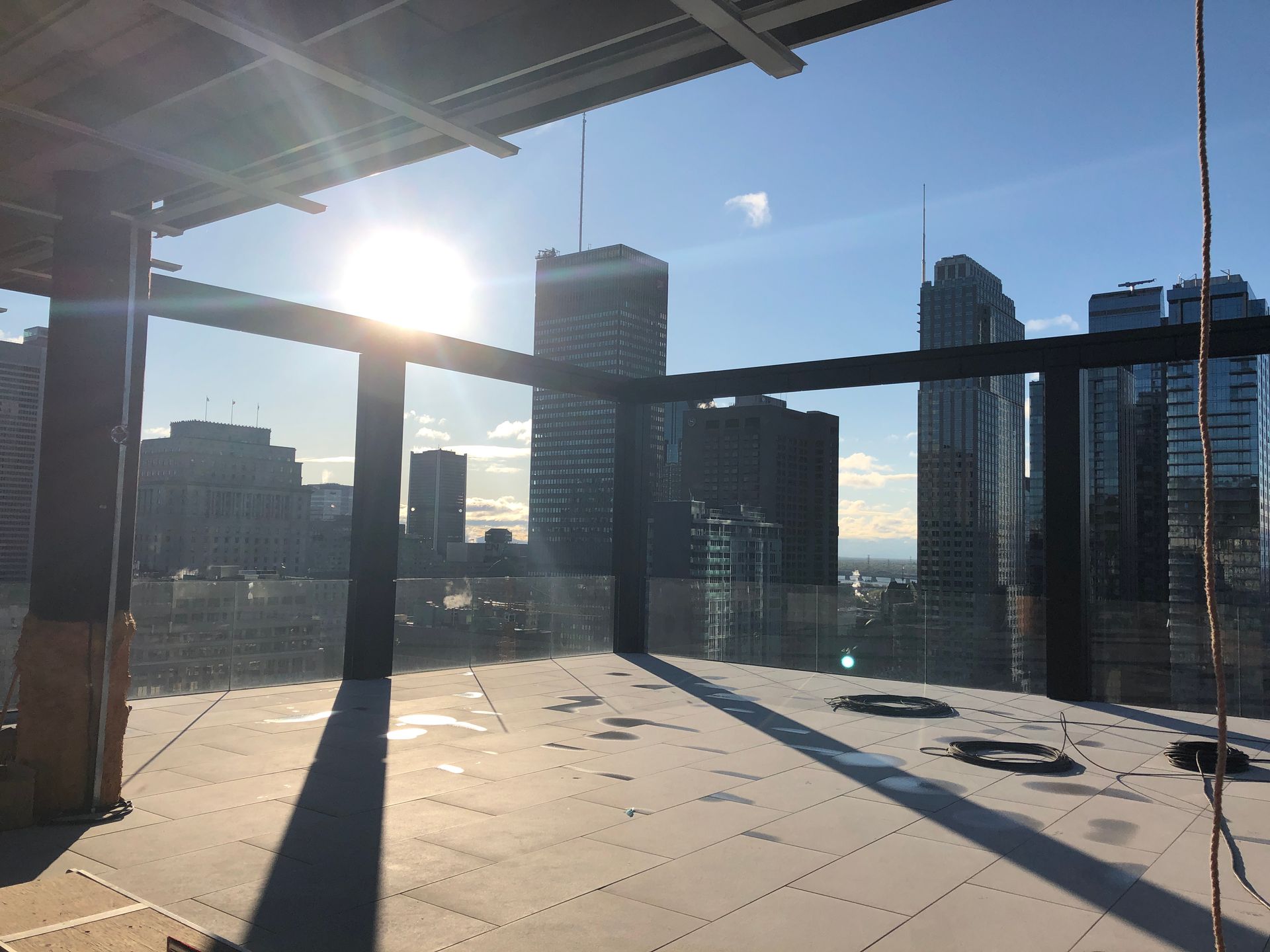 Une terrasse extérieure sur le toit, en construction, avec une structure métallique, offrant une vue imprenable sur la ville au coucher du soleil.