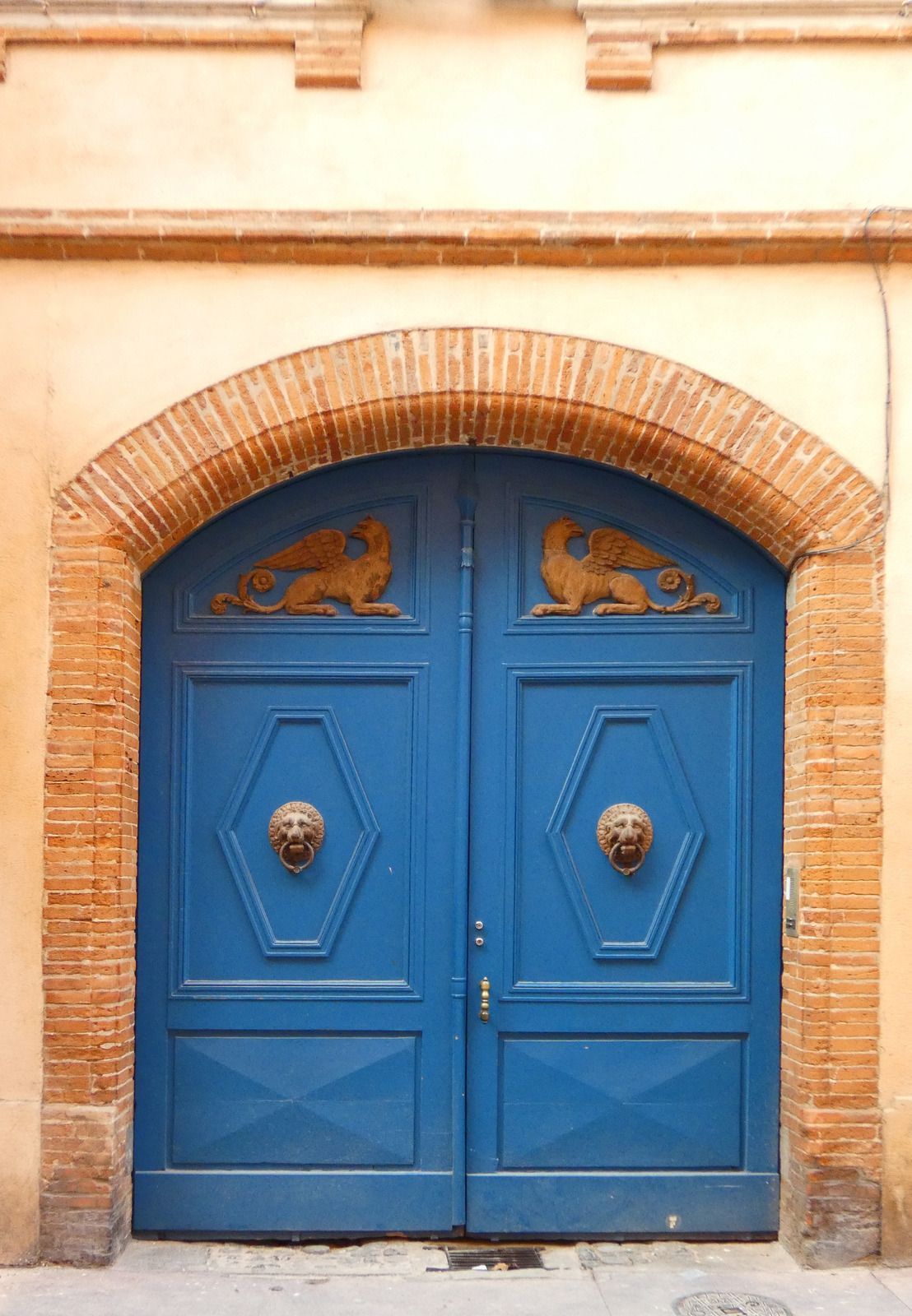 Blue double doors with lion head knockers, ornate carvings, and a brick archway.