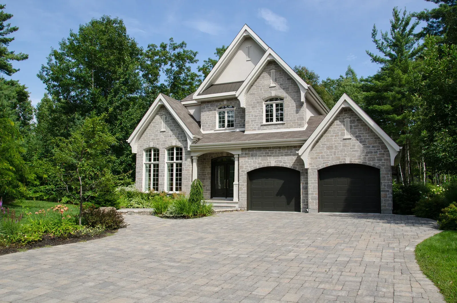 Two-story gray stone house with a driveway and two-car garage, surrounded by trees.