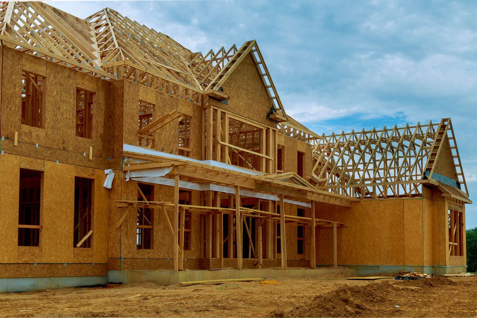 House under construction; wooden frame, exterior walls, and roof structure visible against a cloudy sky.