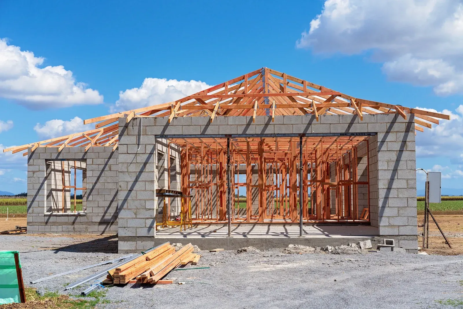 House under construction with concrete block walls, wooden framing, and blue sky.