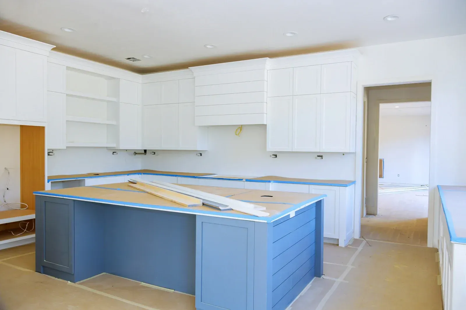 Kitchen remodel in progress, blue island, white cabinets, unfinished countertops, doorway in background.
