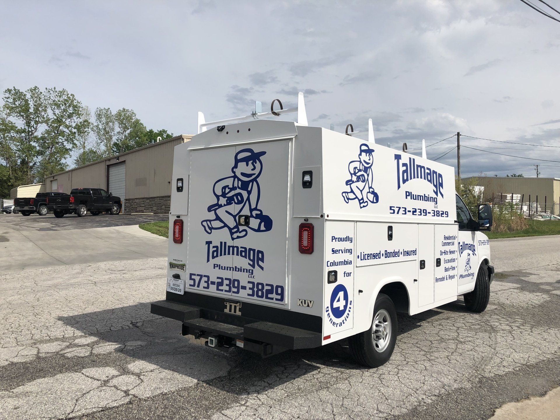 A white truck with a plumber on the back is parked on the side of the road.