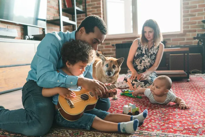 Family playing music on a rug with a child, dog, and baby in a cozy living room