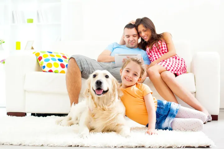 Happy family lounging on a white couch with a golden retriever in a bright living room
