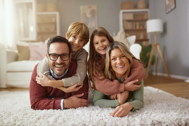 Smiling family of four lying on a white rug in a cozy living room