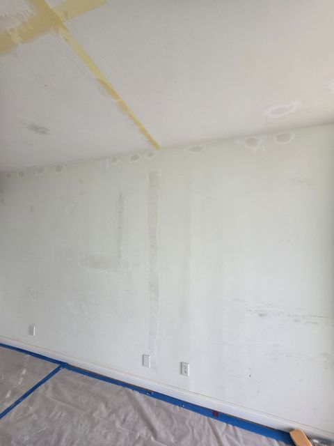 Empty white room wall with blue painter’s tape along the floor and plastic sheeting covering the floor.