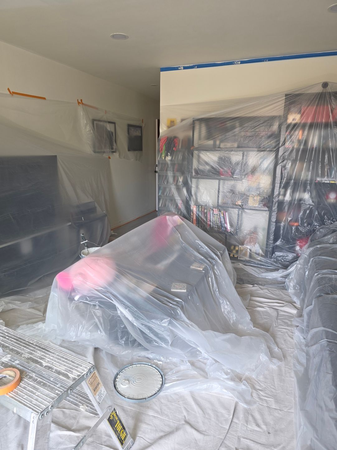 Room under renovation with furniture covered in plastic sheeting and drop cloths