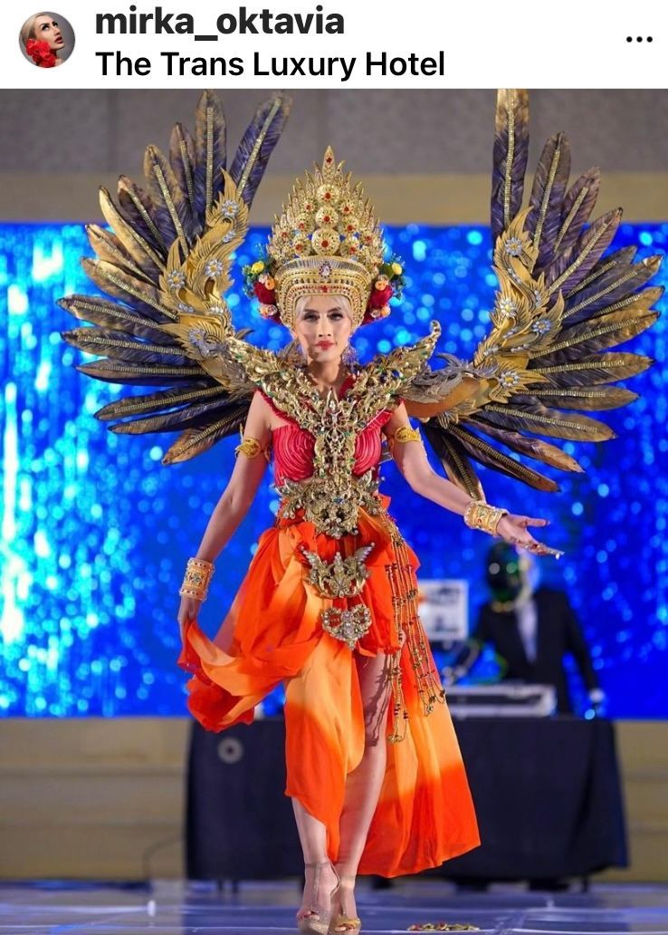Woman in elaborate orange and gold costume with large feathered wings poses on stage.