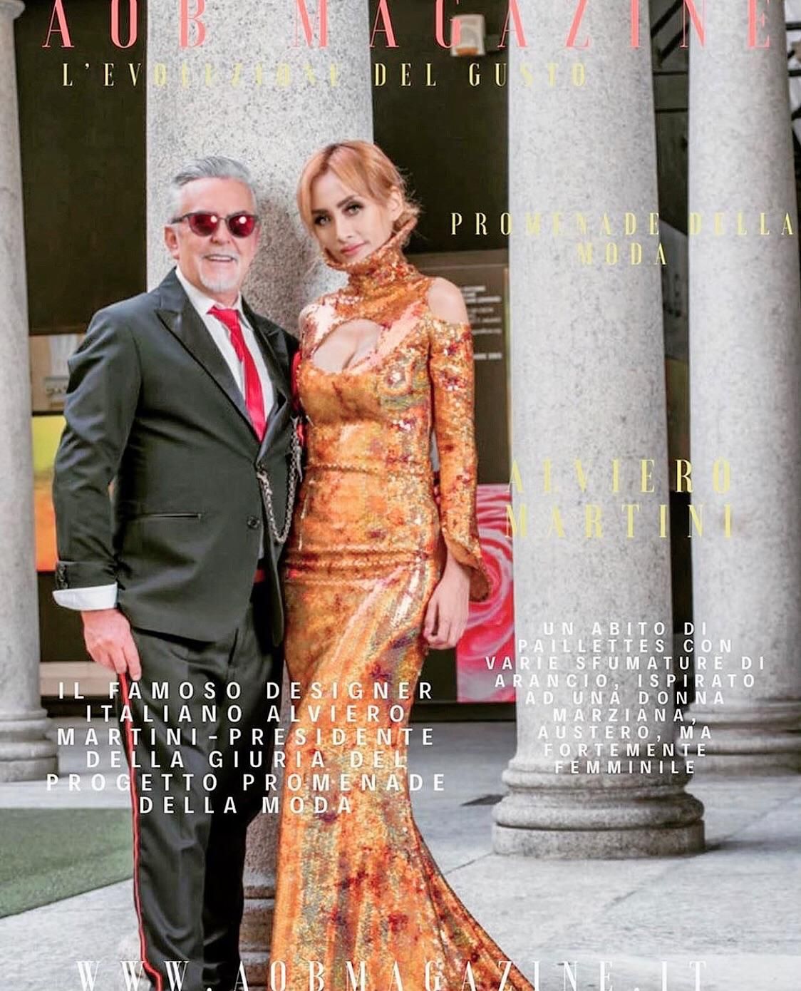 Man and woman pose for magazine cover next to pillars. The woman wears a gold gown and the man wears a suit.
