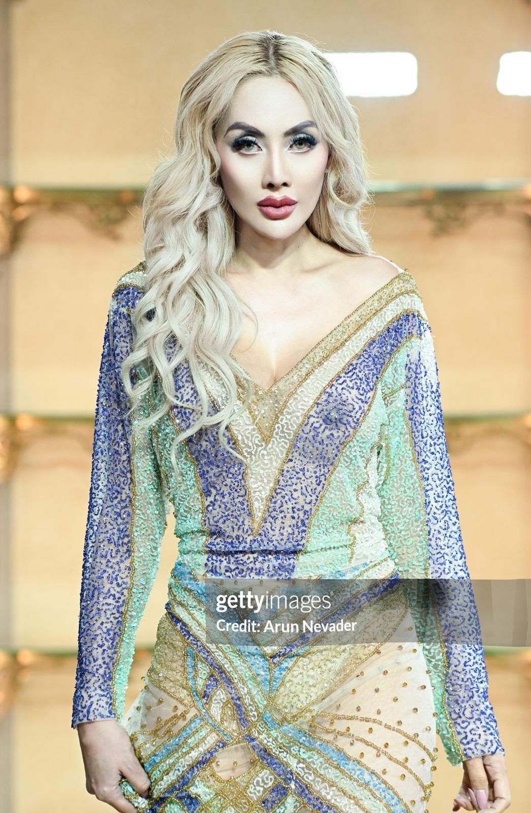 Woman in sparkling gown posing, long blonde hair, bright makeup.