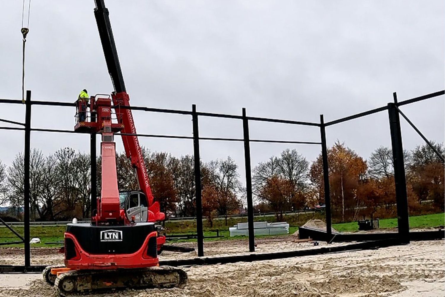 A red crane is being used to build a fence.
