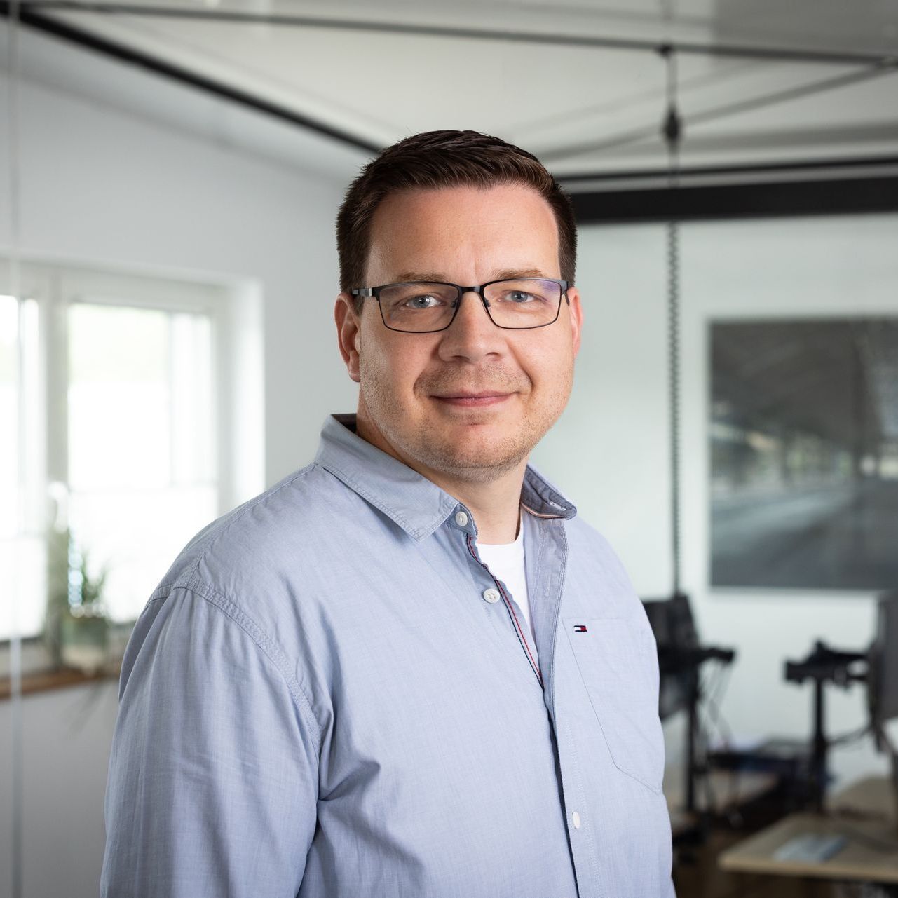 Ein Mann mit Brille und blauem Hemd steht in einem Raum.