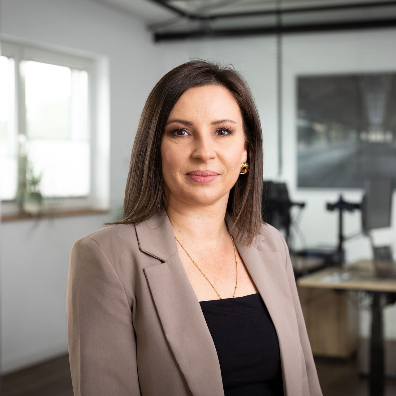 Eine Frau in einer braunen Jacke und einem schwarzen Oberteil steht in einem Büro.