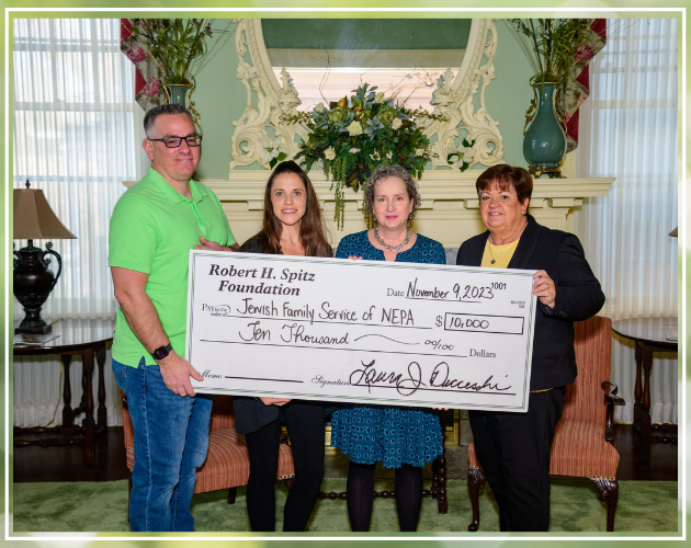Four people holding a large check in a room. Check states $10,000 to Jewish Family Service of NEPA.