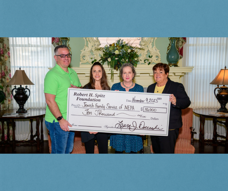 Four people holding a large check in a room. Check states $10,000 to Jewish Family Service of NEPA.