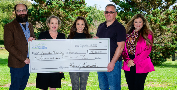 Five people hold a large check for $5,000 made out to