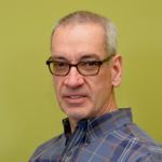 Man with glasses and grey hair wearing a plaid shirt, facing the camera.
