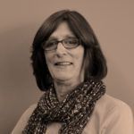 Woman wearing glasses and a scarf, smiling.