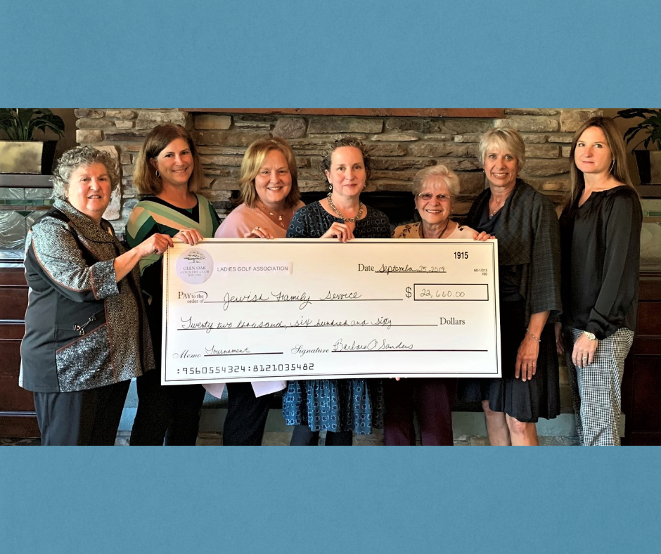 Group of women holding large check in front of a stone fireplace.