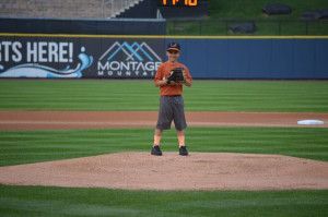 Boy on a baseball mound, wearing a glove and cap, standing in front of a sign that says 