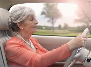 Woman driving a car, holding the steering wheel. She is in a vehicle with a scenic background.