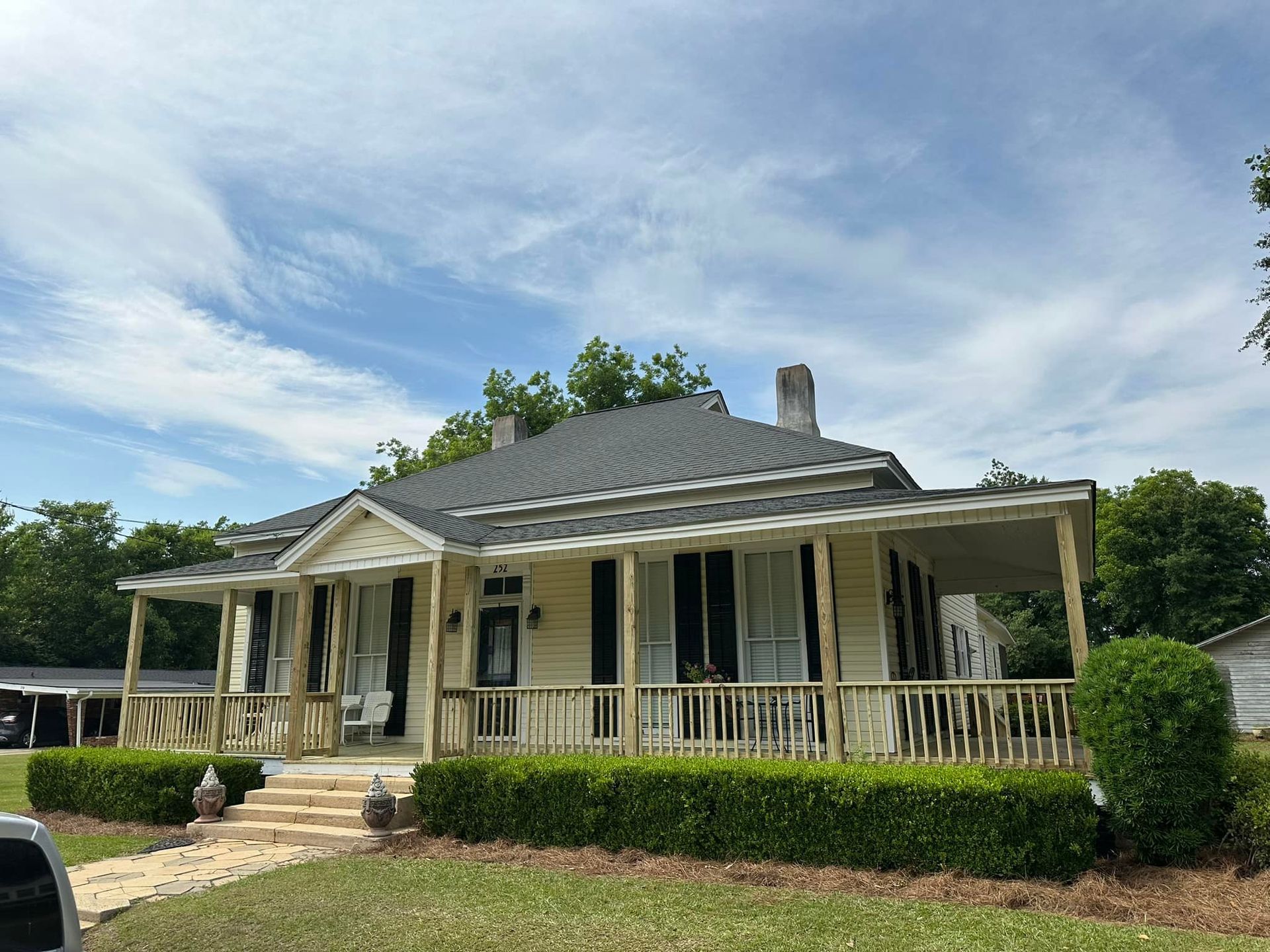 A white house with a large porch and a car parked in front of it.