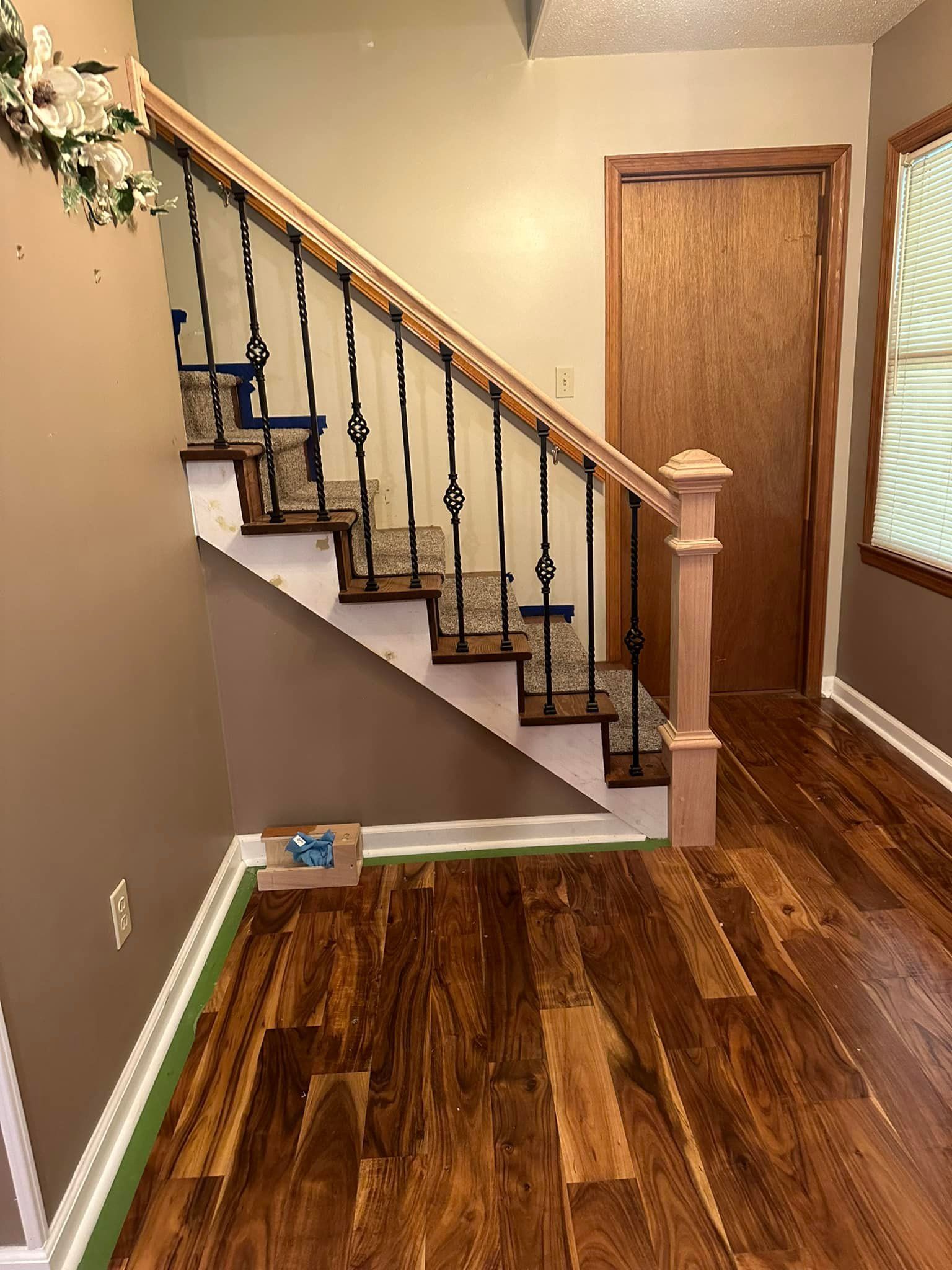 A wooden staircase with a wrought iron railing in a hallway with hardwood floors.