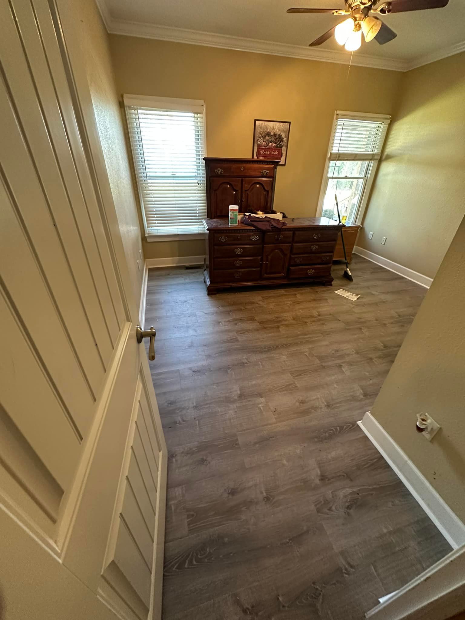 A room with hardwood floors , a dresser , and a ceiling fan.