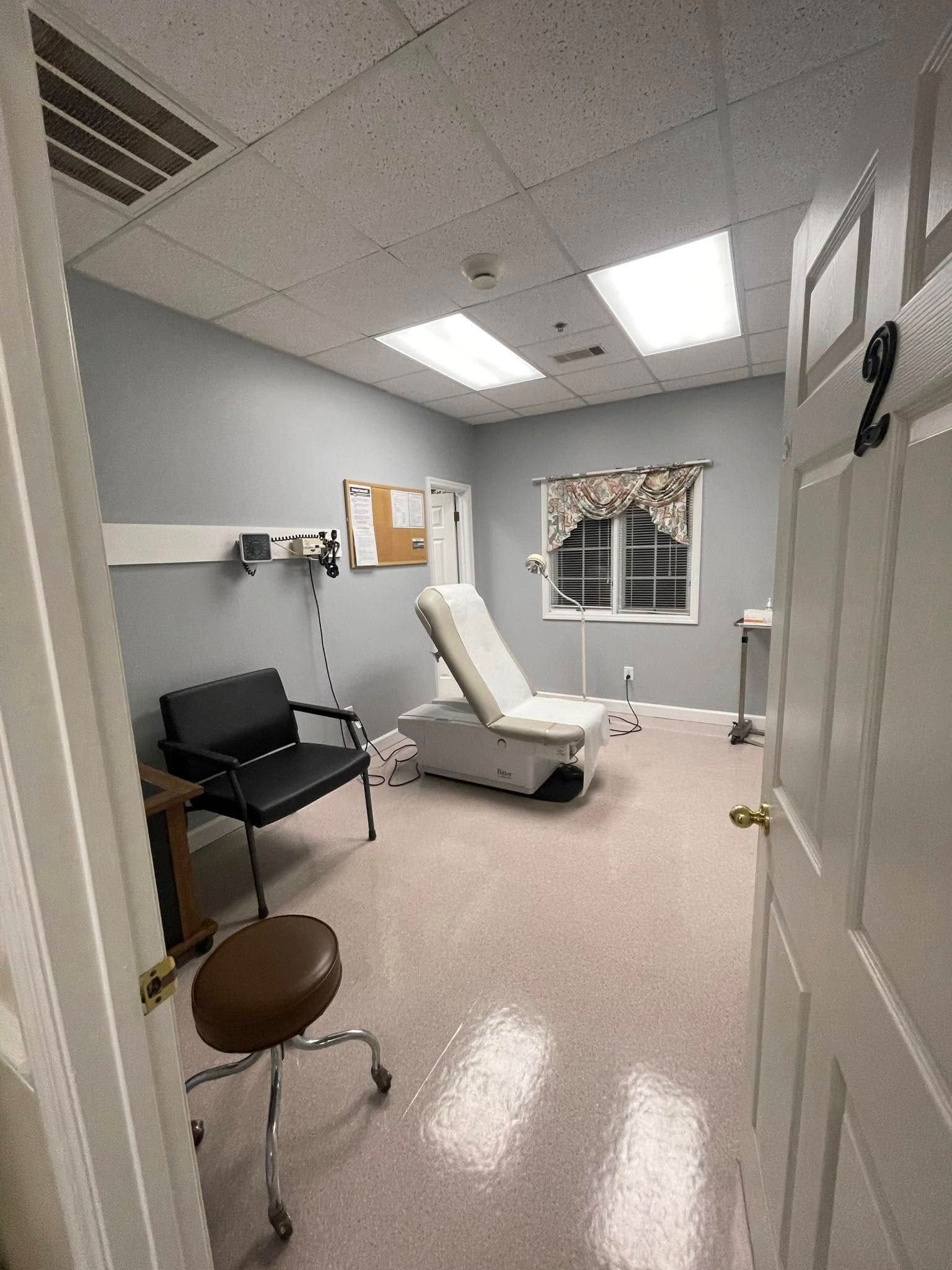A doctor 's office with a chair , stool , and window.