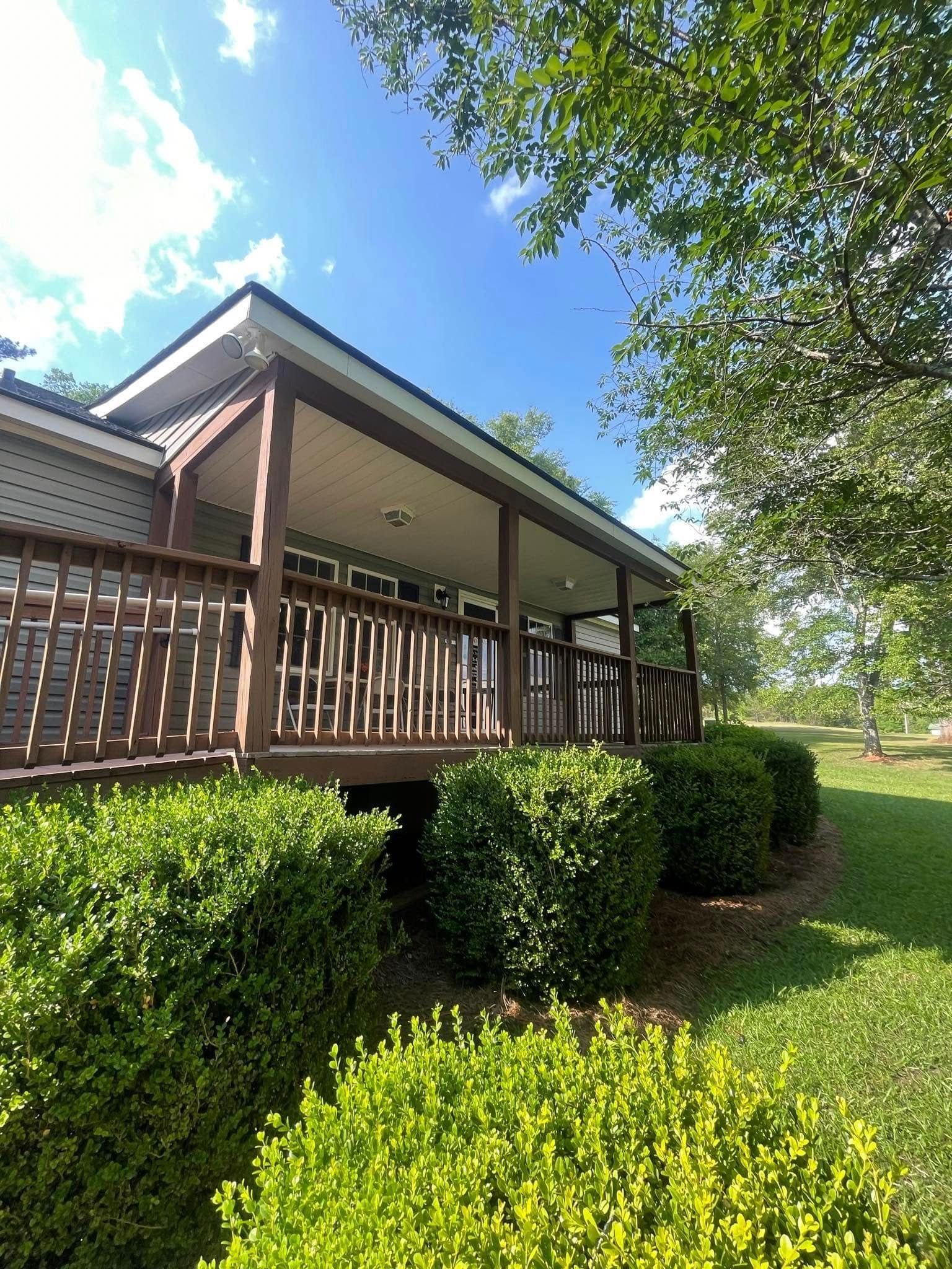 A house with a large porch surrounded by bushes and trees.