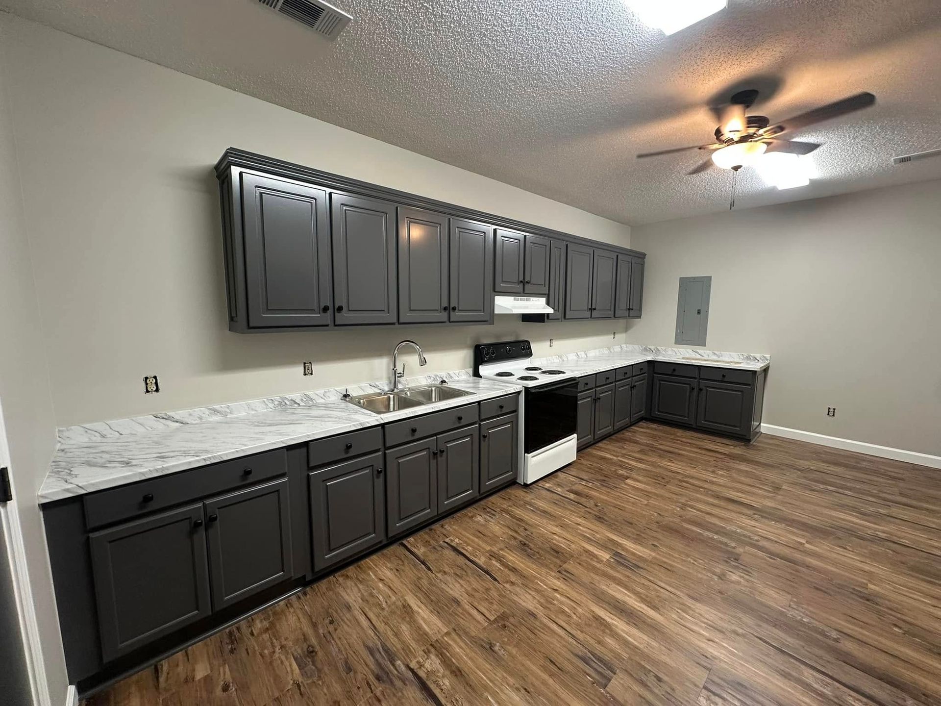 A kitchen with gray cabinets , a sink , a stove , and a ceiling fan.