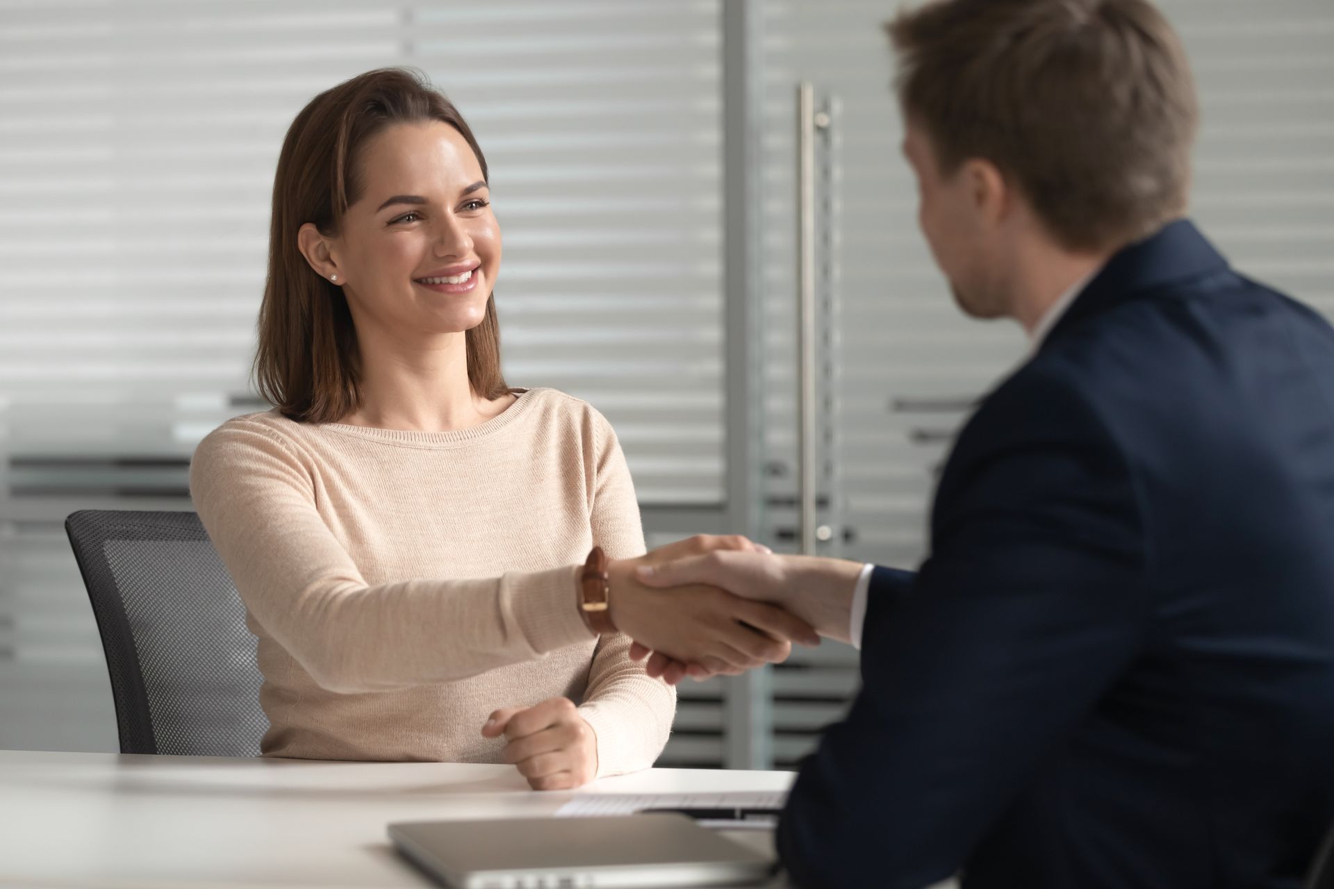 Two people shaking hands across a desk in a bright office