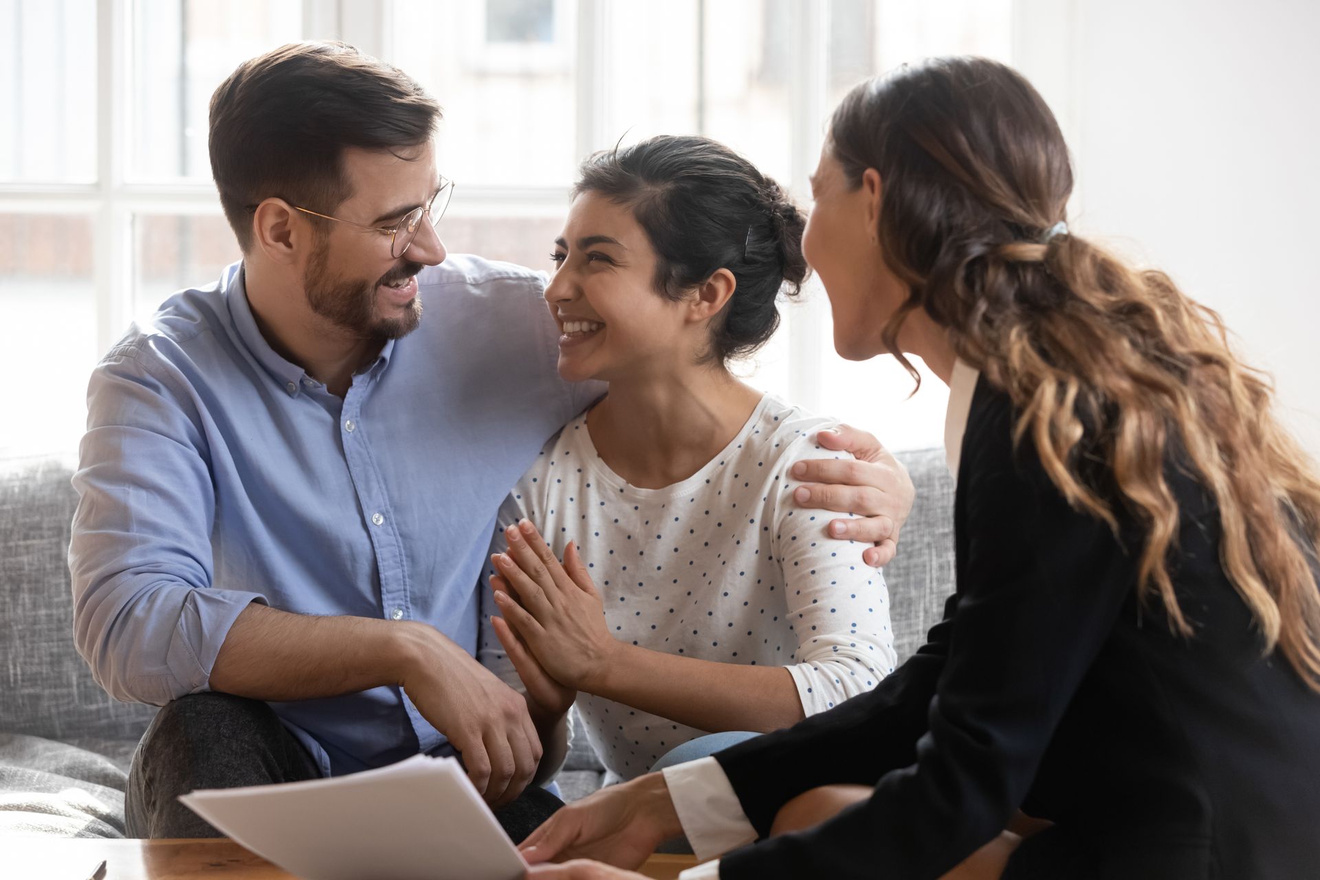 Three people smiling and talking on a couch beside an open laptop