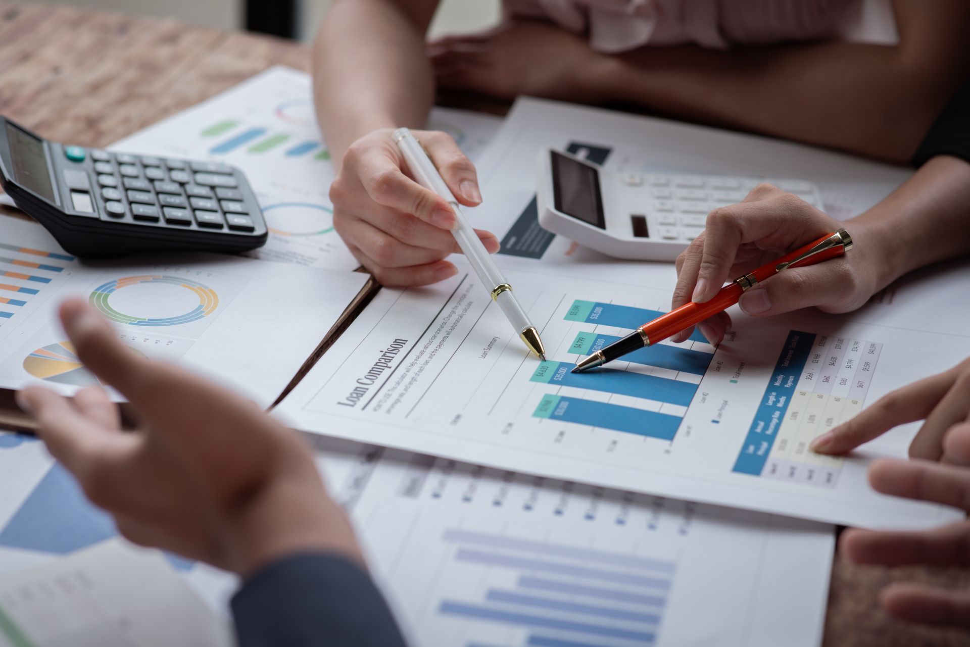 Hands reviewing charts and graphs on a desk, with a calculator and coffee cup nearby