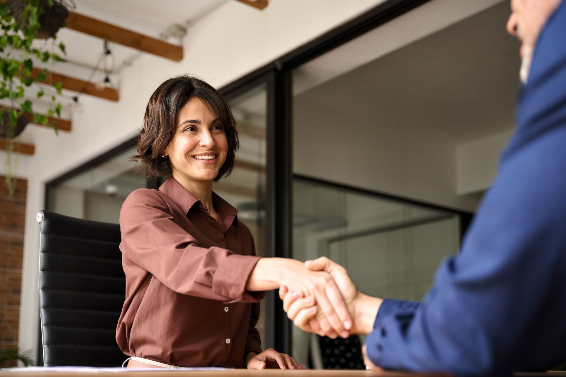 Two people shaking hands in an office, with one smiling behind a desk.