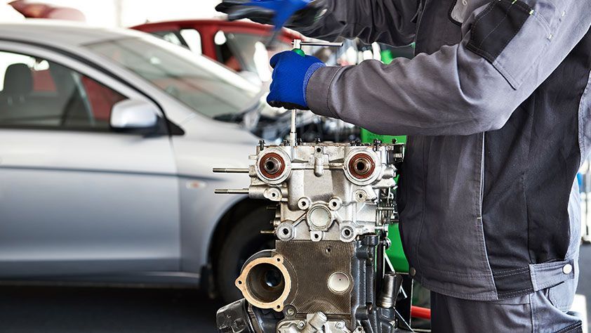 Mechanic in a garage working on an engine beside a silver car | Tinley Auto Repair & Towing Inc