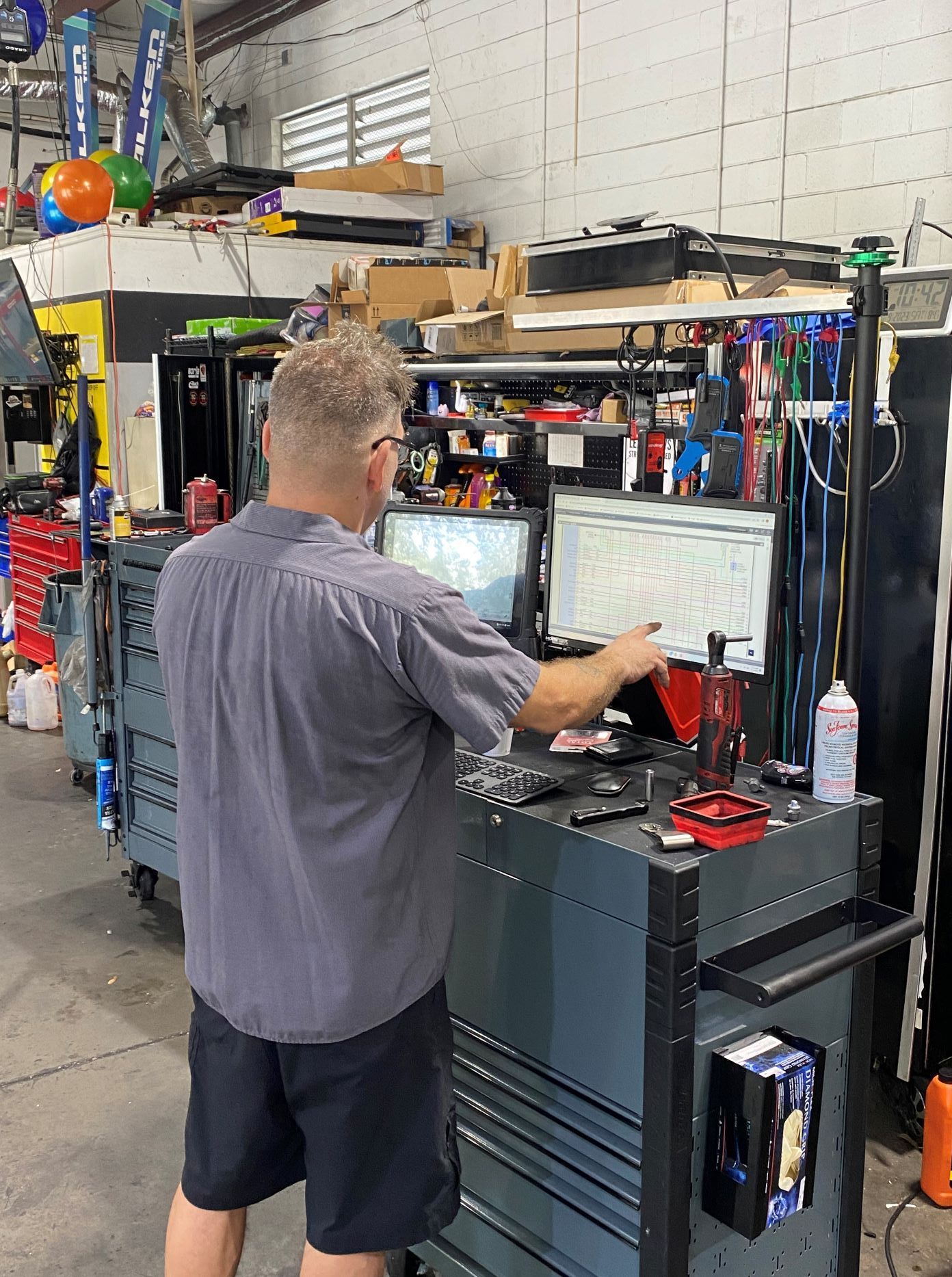 Mechanic examining a car engine in a garage. He is wearing glasses, dark clothes and is focused on the engine.