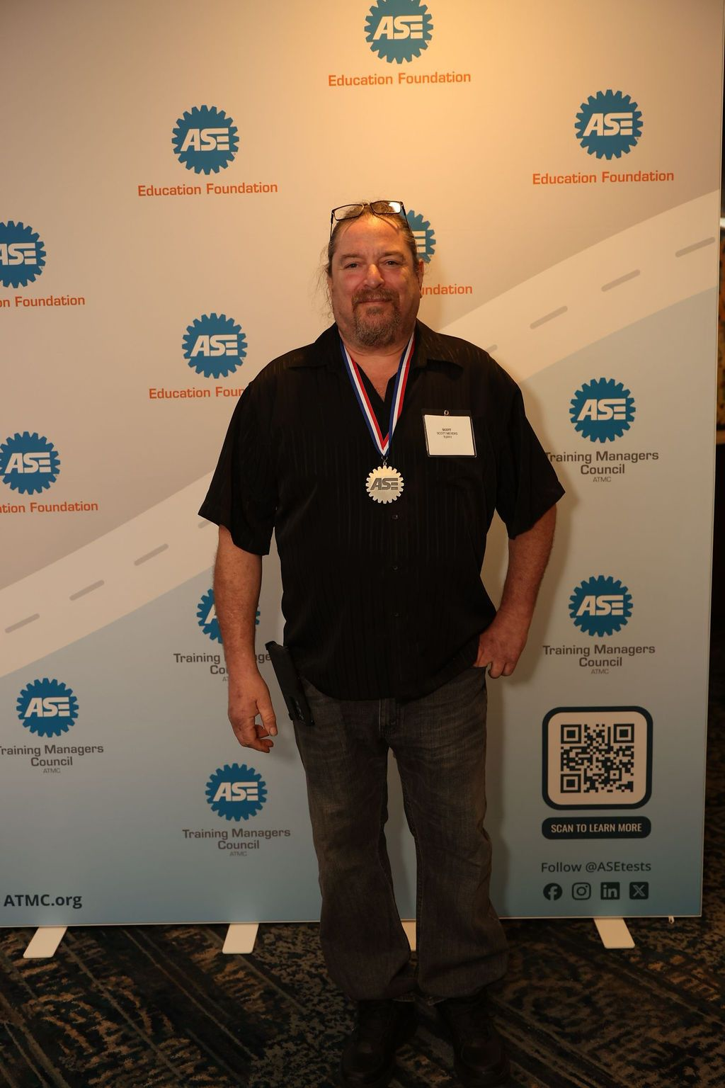 Man in black shirt and medal stands in front of a banner with logos.