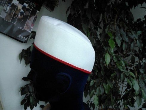 Cappello blu navy con bordi bianchi e rossi su testa di manichino nera, su uno sfondo di fogliame verde.