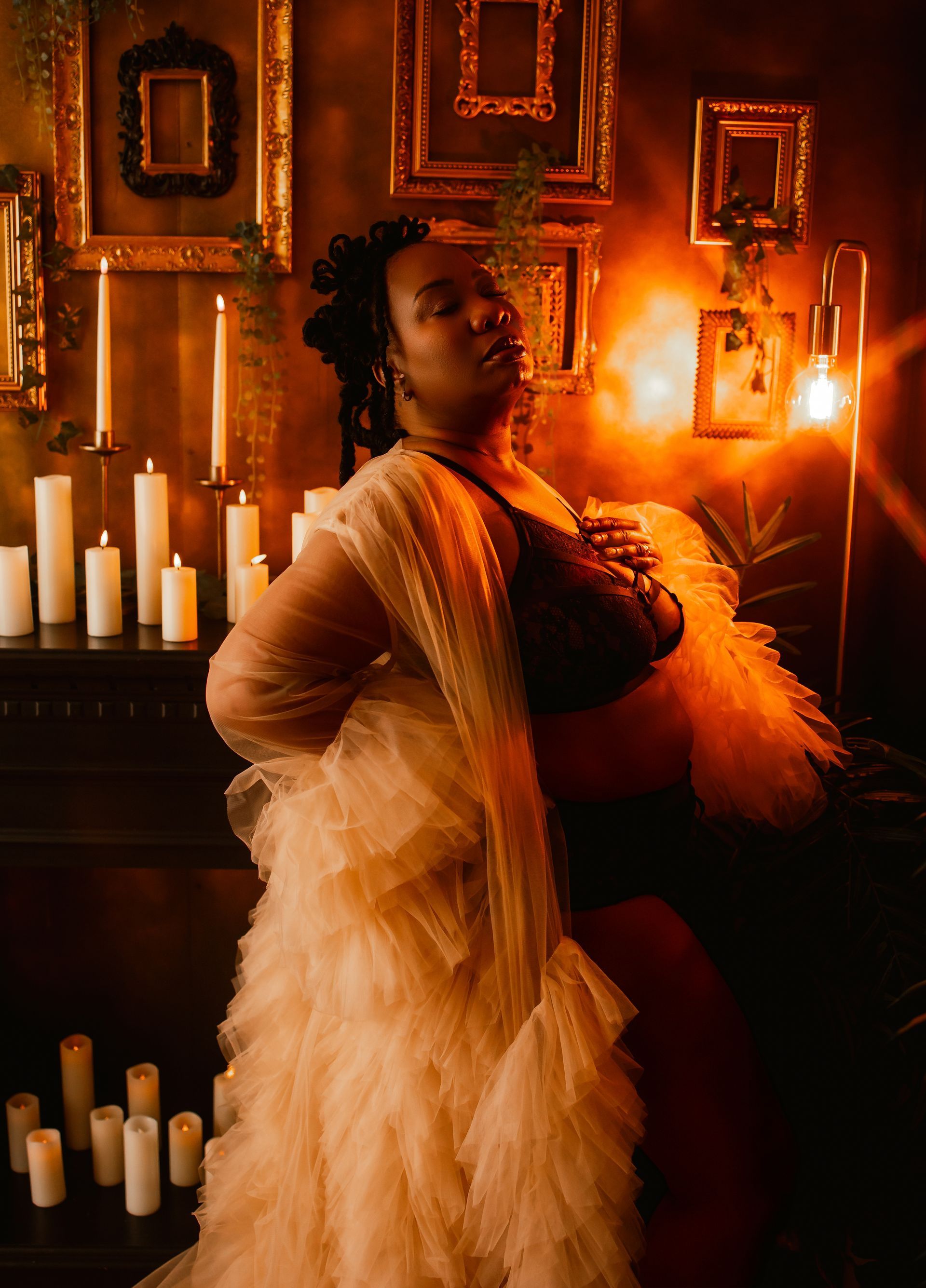 A pregnant woman is standing in front of a fireplace surrounded by candles.
