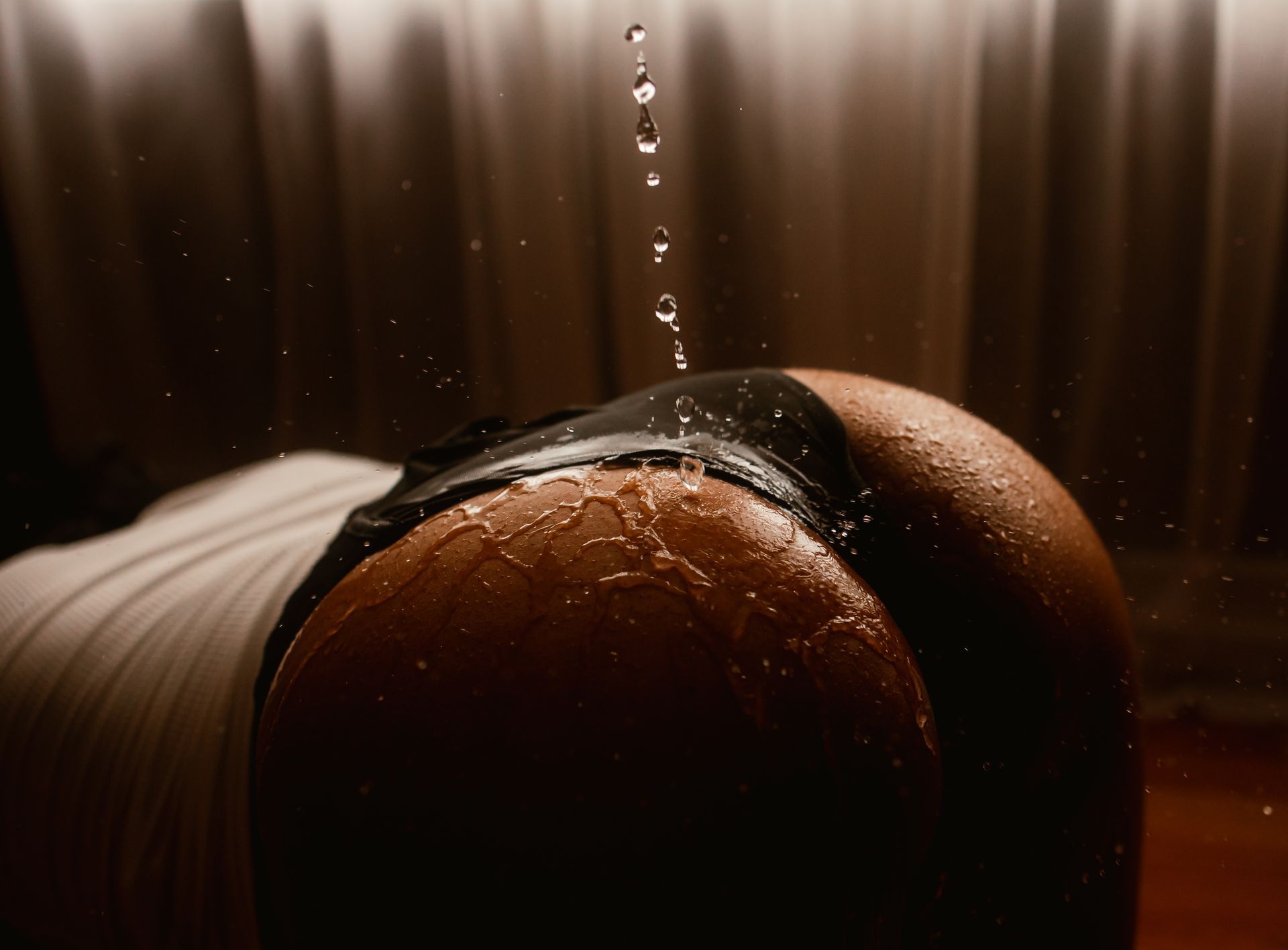 Raindrops falling on a person’s bare back and shoulder in warm, dim light
