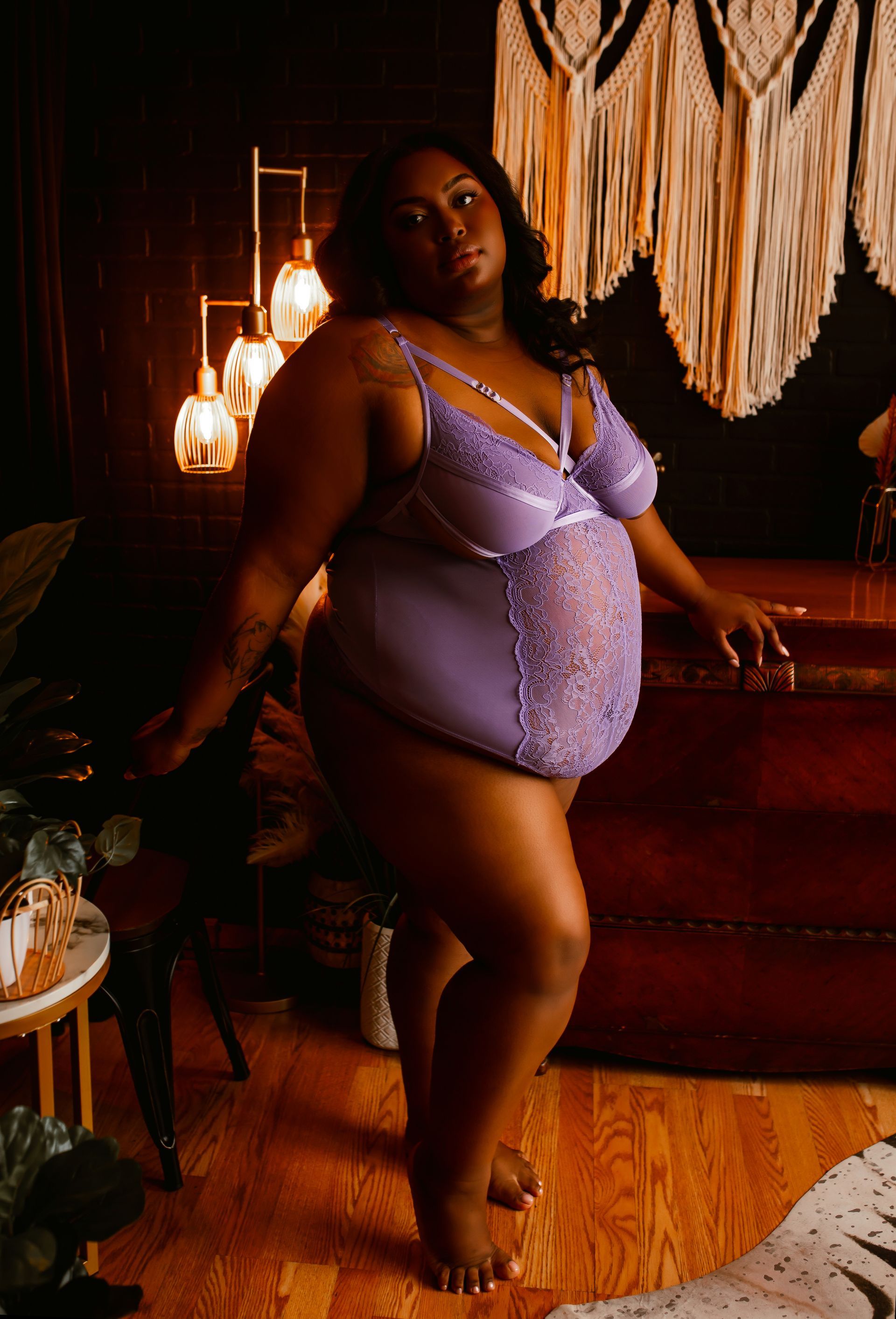A plus size woman is standing in a room wearing purple lingerie.