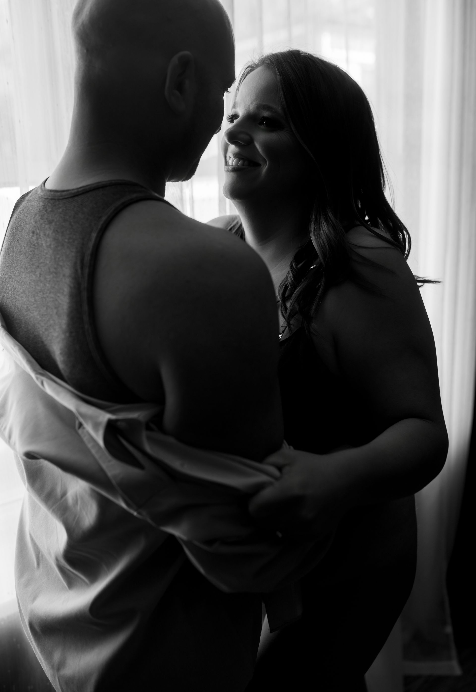 A man and a woman are standing next to each other in front of a window.