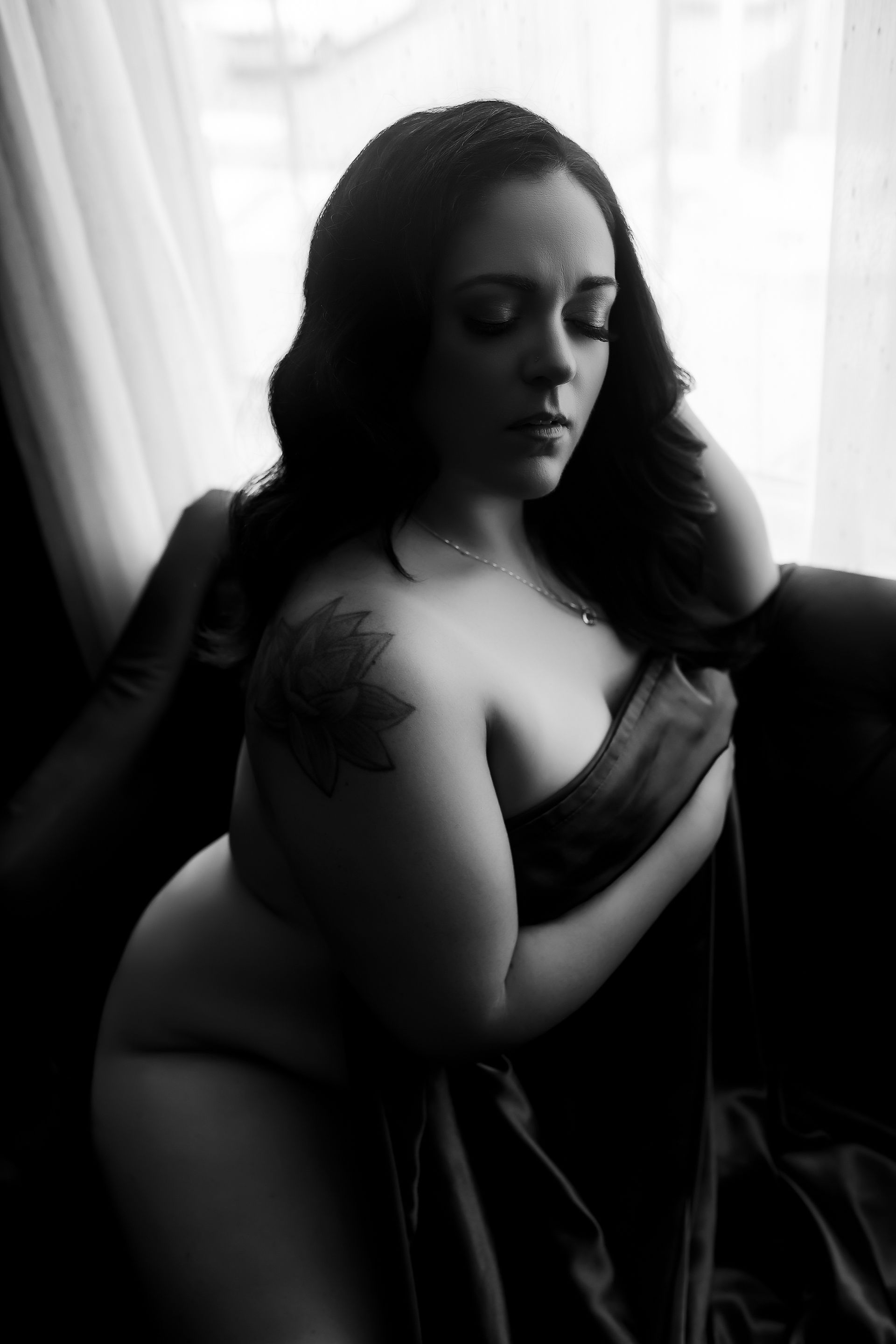 A woman in lingerie is sitting on a couch in front of a window.