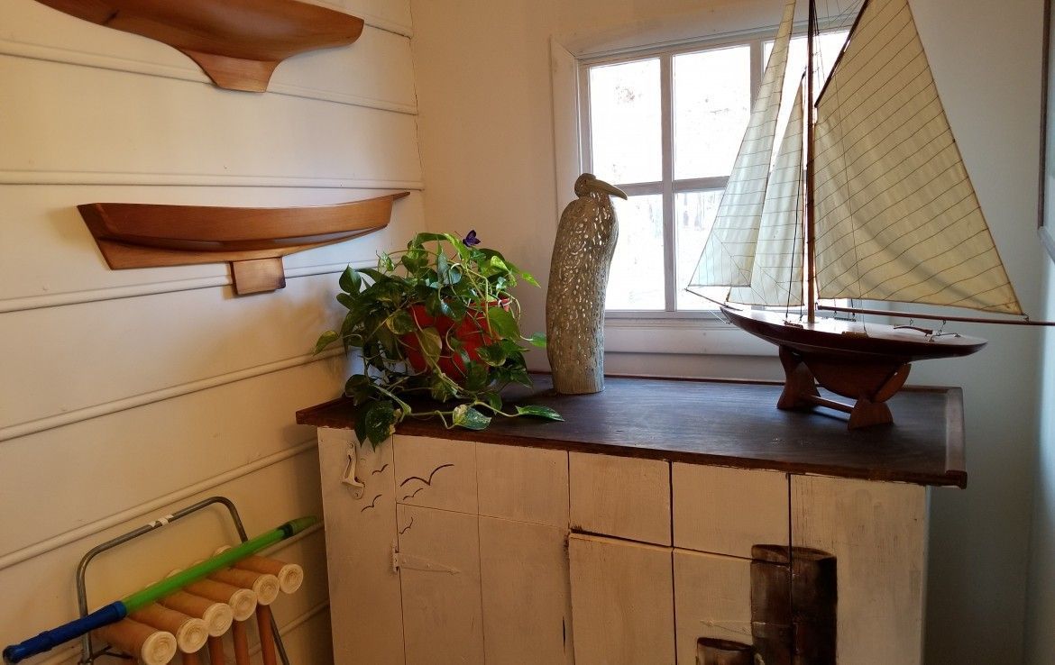 Wooden shelves with boat-shaped decorations, a window with a sailboat, and a cabinet with plants.