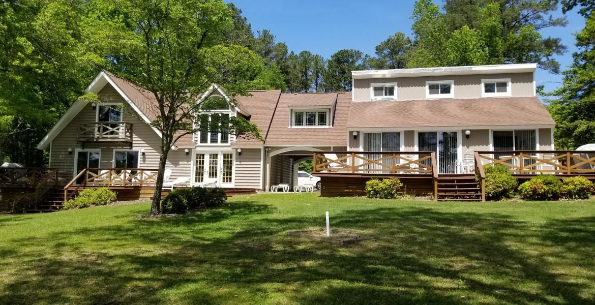 A two-story house with a wooden deck and a green lawn under a sunny sky.