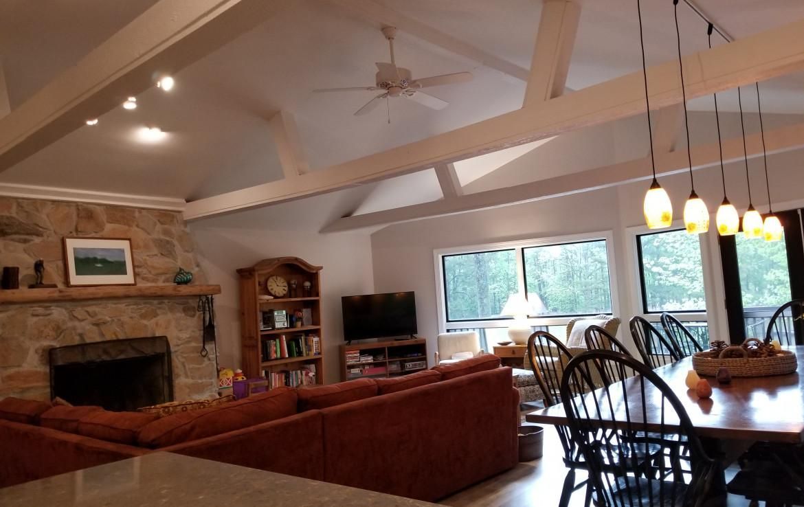 Living room with stone fireplace, red sectional sofa, and dining table with hanging lights.